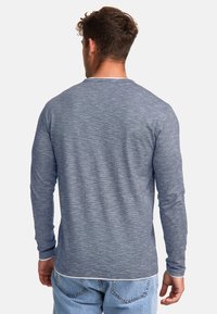 Long-sleeve shirt in dark blue heathered fabric with a crew neckline, straight hem, and ribbed cuffs, styled with casual light blue jeans.