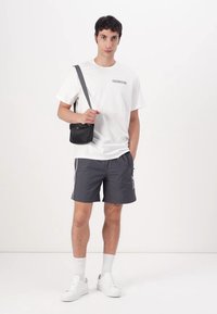 Black crossbody bag, white t-shirt with “Calvin Klein” logo, gray swim shorts with side stripes, white sneakers, and white socks.