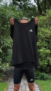 Top atlético preto com um corte solto, apresentando um decote redondo e um logotipo branco na parte frontal. O tecido parece leve e respirável.