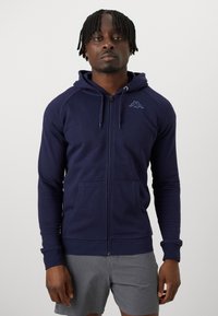 Námornícky zipsový hoodie vyrobený z bavlnenej zmesi, s kapucňou na šnúrku, klokankovými vreckami, rebrovanými manžetami a malým logom na hrudi.