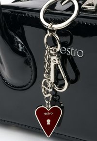 Czarna lakierowana torebka z srebrnymi akcentami, z serduszkowym bordowym breloczkiem z zamkiem i nazwą marki "estro" wyrytą.