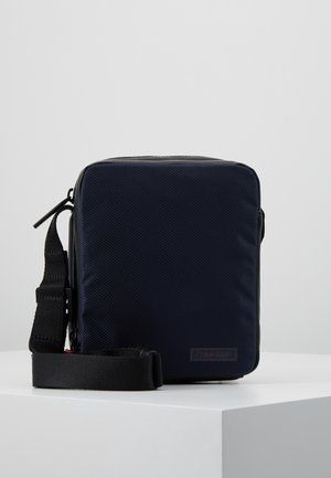 Granatowa prostokątna torebka na ramię z czarnym regulowanym paskiem, teksturowaną przednią częścią i subtelnym logo Calvin Klein w dolnym prawym rogu.