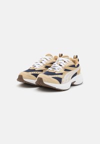 Scarpe da ginnastica beige e blu navy con pannelli in rete, lacci bianchi, suole testurizzate e marchio PUMA di lato e dietro.