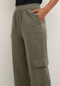 Pantalons cargo vert olive avec une taille élastique, poches latérales et une poche à rabat sur la cuisse. Fabriqués en tissu léger et texturé.
