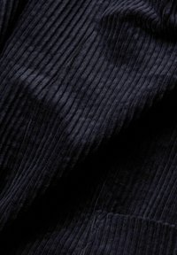 Tissu en velours côtelé bleu marine foncé avec des nervures verticales et une texture douce, légèrement plié montrant la profondeur et les ombres.