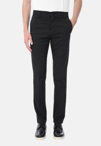 Pantaloni in tessuto nero con vestibilità slim, dotati di chiusura frontale con bottone, passanti per cintura e tasche laterali, abbinati a scarpe eleganti nere.