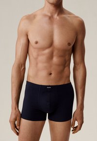 Granatowe bokserki wykonane z miękkiego materiału, z logo na pasku, dopasowanym kroju i gładką teksturą. Model nosi je bez koszulki.