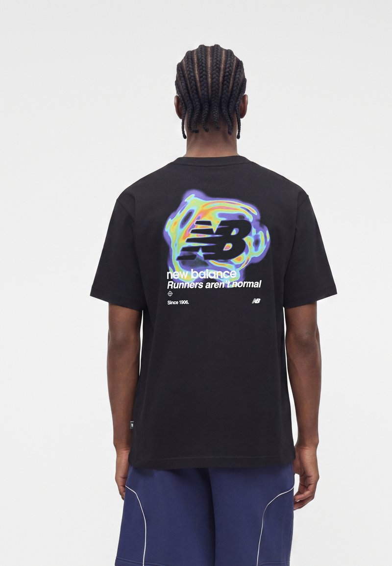 Άνδρας με πλεξούδες που φοράει μαύρο t-shirt New Balance με πολύχρωμο λογότυπο και κείμενο "Runners aren't normal" στην πλάτη, και μπλε σορτς.