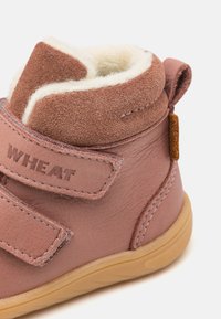Růžová kožená kotníková obuv s měkkým krémovým podšívkou, semišovými prvky, suchými zipy a gumovou podrážkou. Logo "WHEAT" je embosováno na pásku.