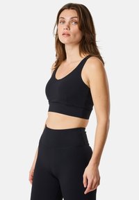 Svart sportbustier med V-ringning och breda axelband, tillverkad av ett mjukt och elastiskt material. Kombineras med högmidjade svarta leggings.
