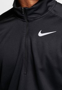 Nike musta vetoketjullinen takki, kohokuvioitua kangasta, etuosan puolivetoketju ja valkoinen logo vasemmassa rinnassa. Suunniteltu urheilukäyttöön.