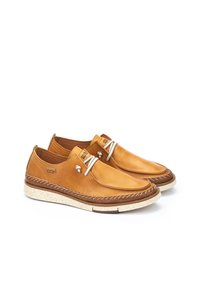 Zapatos de cuero color miel con un acabado suave, que cuentan con una suela marrón en contraste, costuras decorativas y elementos metálicos para los cordones.