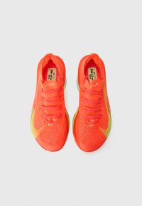 Neon orange atletiske sko med en mesh-overdel, reflekterende detaljer og en kontrasterende grøn sål. Har flade snørebånd og en polstret indersål.