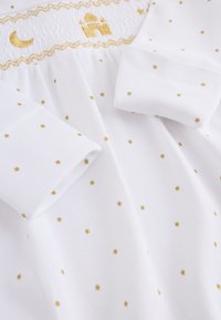 Tenue bébé blanche avec étoiles dorées, manches retroussées et encolure smockée avec broderies dorées de lune, étoile et château.