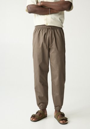 Brown drawstring pants with elastic cuffs; lightweight cotton fabric; paired with olive green sandals featuring a buckle detail.