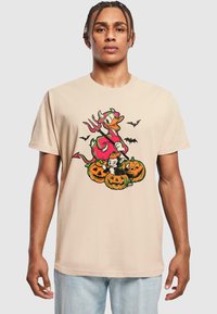 Beige Baumwoll-T-Shirt mit einem bunten Halloween-Motiv, das einen rosa Charakter, Kürbisse und Fledermäuse zeigt. Kurze Ärmel und lockere Passform.