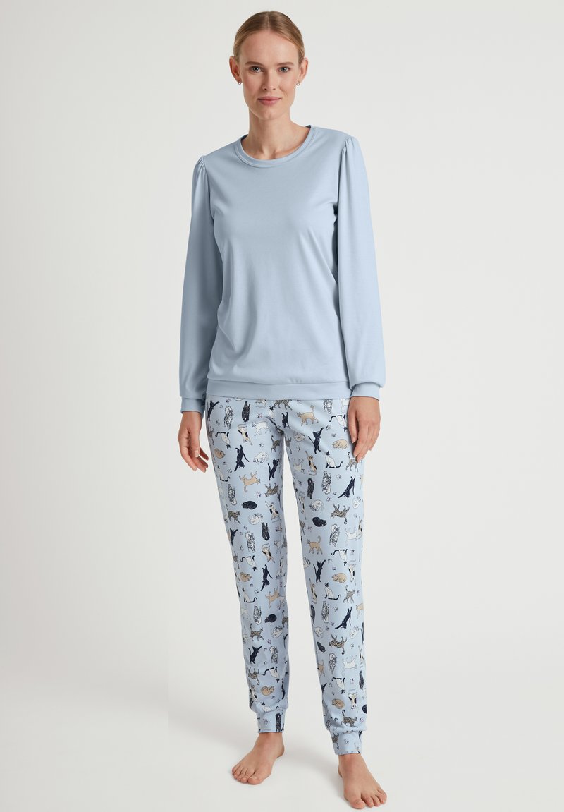 Hellblaues Langarmoberteil mit gepufften Schultern, kombiniert mit blauen Schlafanzughosen mit einem verspielten Tiermuster in Dunkelblau und Beige.