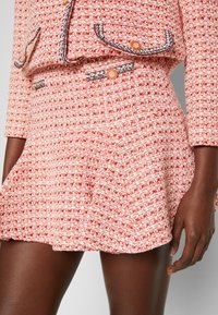 Traje de tweed con textura en rojo y blanco, compuesto por un chaleco ajustado y una falda acampanada. Presenta botones decorativos y detalles de costura contrastantes.