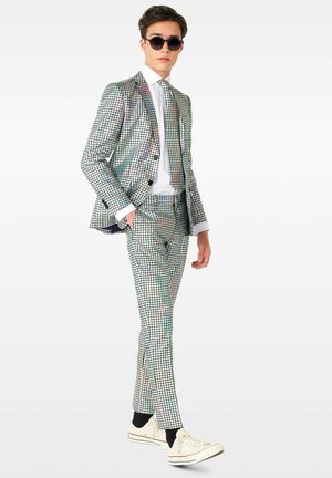Costume à carreaux multicolores en matériau réfléchissant, à coupe ajustée, associé à une chemise blanche et des baskets. Lunettes de soleil noires portées.