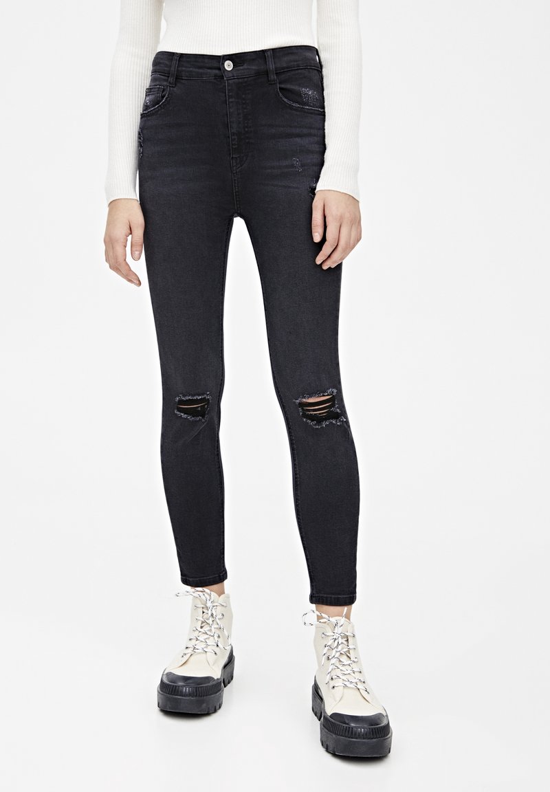 Jeans ajustados negros de cintura alta, con dos rotos en las rodillas, hechos de denim, combinados con botas negras de plataforma con cordones.
