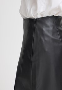 Schwarzer Lederrock mit glatter Textur, hoher Taille und vertikalen Nahtdetails. Reißverschlussverschluss hinten.