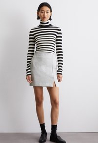 Schwarz-weiß gestreifter Rollkragenpullover, grauer taillierter Minirock mit seitlichem Schlitz, schwarze Socken und schwarze flache Schuhe. Glatte Textur und einfaches Design.