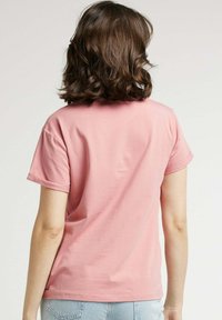 T-shirt en coton rose avec des manches courtes roulées, un col rond et une coupe décontractée. Texture lisse et design simple, idéal pour une tenue décontractée.
