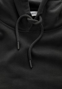 Schwarzer Hoodie aus strukturiertem Stoff, mit einer vorderen Tasche und verstellbarem Kordelzug. Die Enden des Kordelzugs sind aus schwarzem Kunststoff.
