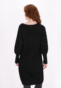 Schwarzes gestricktes Sweaterkleid mit langen Puffärmeln, strukturiertem Muster an den Ärmeln und einem gerippten Abschluss am Körper. Rundhalsausschnitt.
