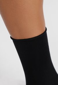 Schwarz Baumwollsocke mit einem glatten, eng anliegenden Schnitt und einem gerippten Bündchen, das gerade über einem gebräunten Knöchel sitzt und ein nahtloses Design präsentiert.