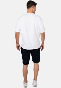 T-shirt bianco in cotone con maniche corte, abbinato a pantaloni corti blu navy. L'outfit presenta una vestibilità casual e scarpe da ginnastica con suola in gomma.