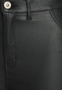 Tecido de denim preto com uma textura suave, apresentando um bolso frontal, ornamento em botão e costura tonal. Design ajustado com um aspeto clássico.