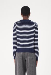 Sweter w niebiesko-białe paski z okrągłym dekoltem, ściągaczami przy rękawach i na dole. Materiał wydaje się miękki, z luźnym krojem. Widok tylko z tyłu.