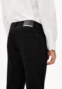 Zwarte denim jeans met een slim fit, met twee achterzakken en een leren label met "ARMEDANGELS" op de tailleband.