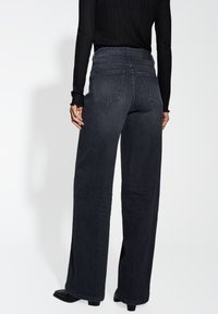 Jean en denim noir taille haute avec des jambes larges, deux poches arrière et une texture lisse, associés à un haut noir moulant en côtes.