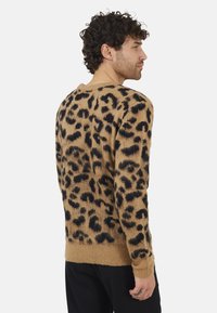 Pull en imprimé léopard marron avec un design tricot texturé. Il possède des manches longues et un col rond. Motif arrière visible et finition des ourlets.