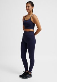 Reggiseno sportivo blu navy e leggings a vita alta con texture a coste. Gamba aderente, indossati con scarpe da ginnastica nere. Design semplice e funzionale.