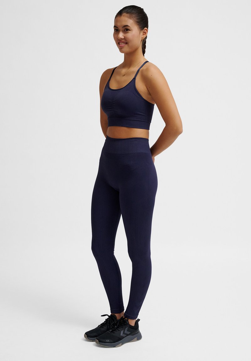 Reggiseno sportivo blu navy e leggings a vita alta con texture a coste. Gamba aderente, indossati con scarpe da ginnastica nere. Design semplice e funzionale.