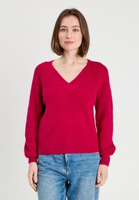 Suéter de punto de manga larga con escote en V en un brillante color rosa, con un acabado texturizado; combinado con jeans de mezclilla azul claro.