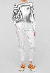 Maglione a righe bianco e blu navy, abbinato a pantaloni bianchi slim fit. Sneakers marroni con dettagli testurizzati e suole in gomma crema.