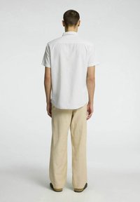 Kortärmad vit skjorta med ett subtilt texturerat mönster, kombinerad med ljusbeige vida byxor och mörkbruna skor.