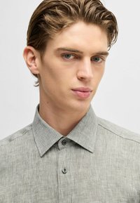 Camicia di lino grigio chiaro con colletto a punta e due bottoni, caratterizzata da un tessuto testurizzato e un sottile motivo a tessitura.