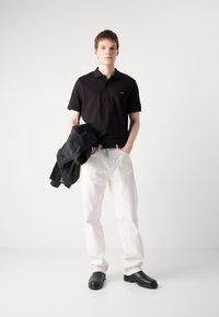 Sort polo-shirt, hvide denim-bukser og sorte sko. En sort jakke ligger over den ene arm. Simpelt design uden fremtrædende mønstre.