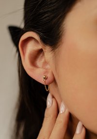 Goldene Ohrcuff mit einer sphärischen Perle und einer Kettendetail, die am Ohrläppchen befestigt ist, mit glatten, polierten Oberflächen und einem zarten Design.