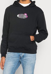 Svart hoodie med en framficka, med en flerfärgad "ADIDAS"-logotyp. Materialet verkar mjukt med en klassisk passform och justerbar dragsko i huvan.