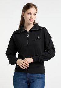 Zwarte sweatshirt met hoge kraag en ritssluiting, met een logo op de linkerborst en geribde manchetten. Zachte textuur en relaxte pasvorm.