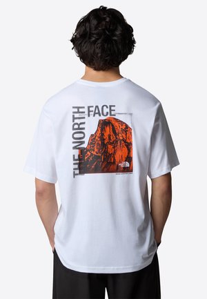 Hvid bomuld t-shirt med et stort orange og sort grafisk motiv af et bjerg på ryggen, med "THE NORTH FACE" tekst og et slogan.