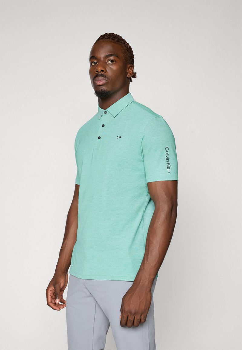 Mintgrünes Polohemd mit kurzen Ärmeln, featuring einen spitzen Kragen, drei schwarze Knöpfe und dem "Calvin Klein" Logo auf dem Ärmel.