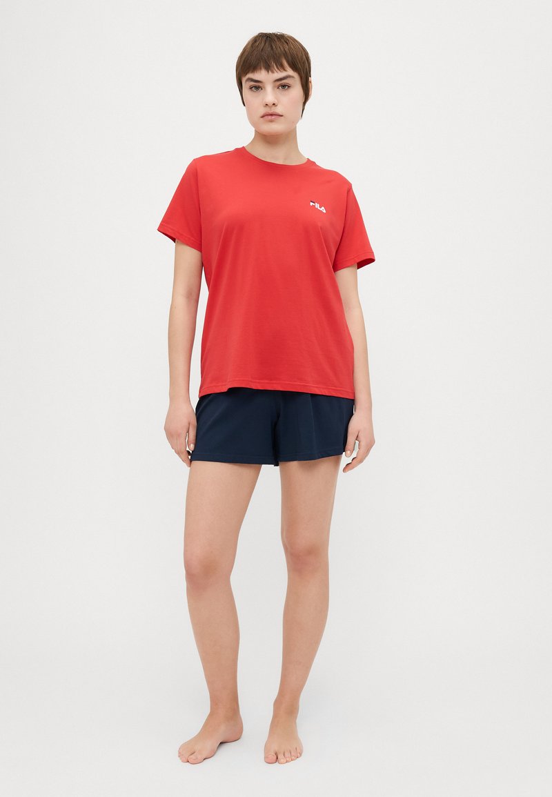 Czerwona koszulka z krótkim rękawem z małym białym logo, w połączeniu z granatowymi szortami. Miękka tkanina, luźny krój, prosty design bez wzorów.