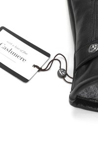 Black leather glove with cashmere lining, featuring a silver button and a tag that reads "with a hint of fine Cashmere."